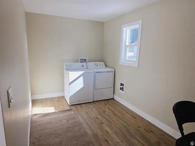 Laundry area featuring wood-finish flooring, light neutral-toned walls, and white baseboards