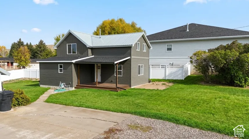 Two-story residence featuring charcoal horizontal siding, a light-colored metal roof, covered front porch, and a white vinyl perimeter fence