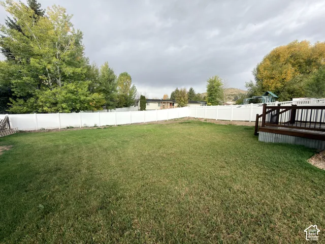 Expansive backyard featuring a manicured lawn, full-perimeter white vinyl fencing, and a raised wooden deck with metal skirting