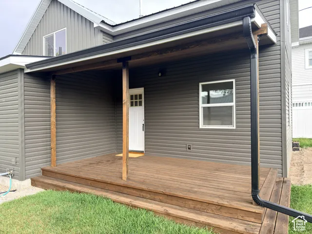 Covered wooden deck featuring natural-finish support posts, gray horizontal siding, and a multi-lite entry door