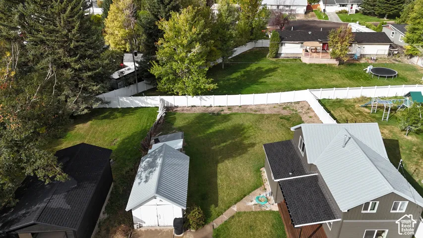 Expansive backyard featuring a white vinyl privacy fence, a detached storage structure, metal roofing, and mature trees