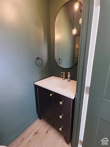 Powder room featuring a dark wood vanity with a white countertop and integrated sink, gold-tone faucet, oval wall mirror, and wood-finish flooring
