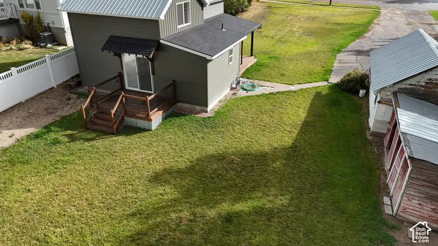 Exterior grounds featuring a wood-deck platform with railing, white vinyl privacy fencing, metal roof accents, and a detached outbuilding