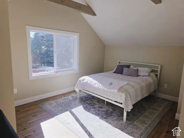 Bedroom featuring wood-finish flooring, a white trim window, sloped ceilings, and exposed wood beams