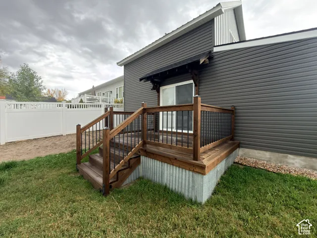 Exterior wood deck featuring black metal balusters and stairs, corrugated metal skirting, and a gable-roofed awning over a sliding glass door