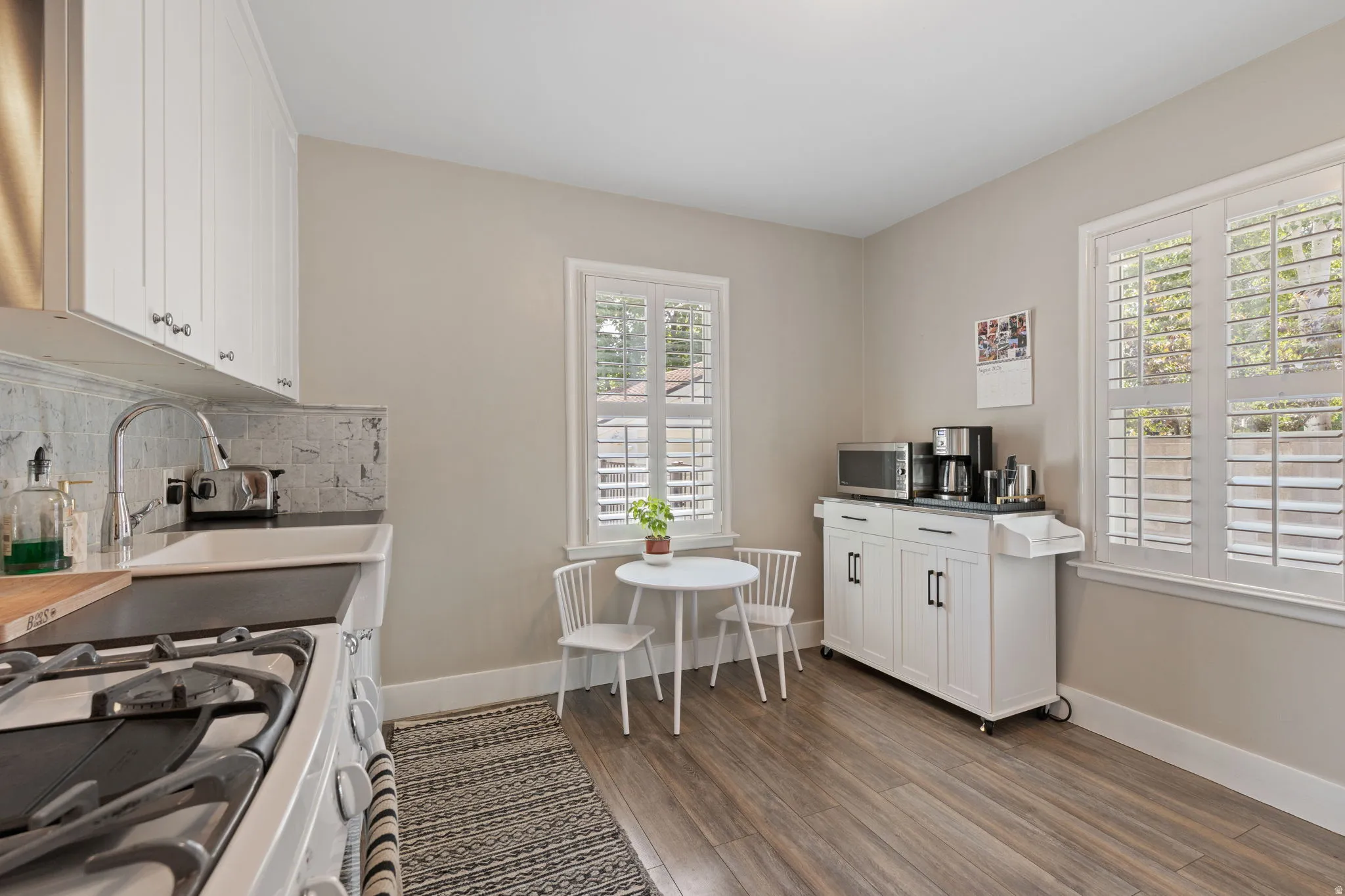 Kitchen featuring wood-finish flooring, white cabinetry, a built-in sink, and white window shutters