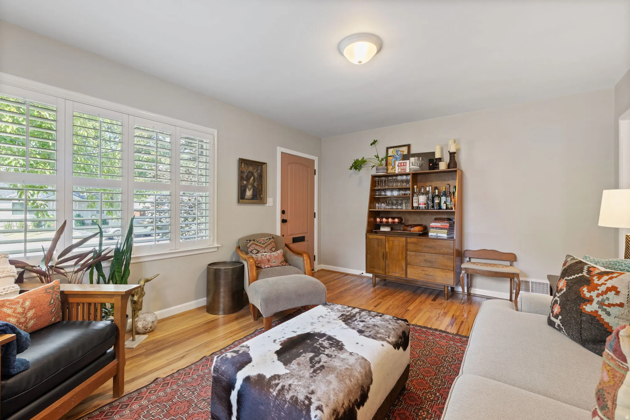 Bright, light-filled living space showcasing hardwood flooring, plantation shutters along expansive windows, and a curated mix of built-in cabinetry and shelving