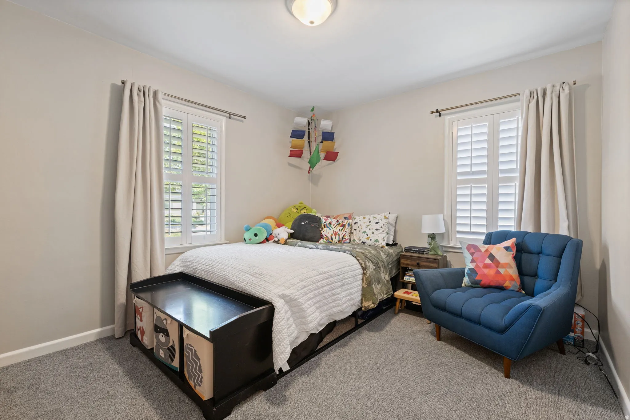 Bedroom featuring two windows with white plantation shutters, neutral wall paint, and gray carpet flooring