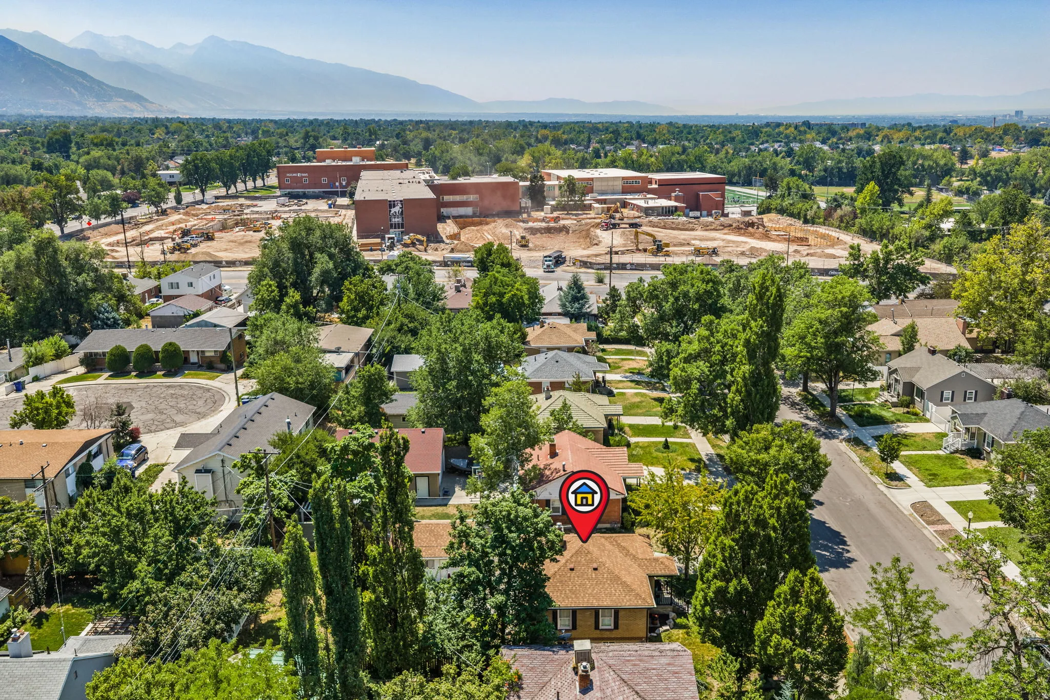 Aerial view showcasing this residential property nestled within a tree-lined neighborhood, featuring mature landscaping, established grounds, and proximity to commercial and institutional buildings