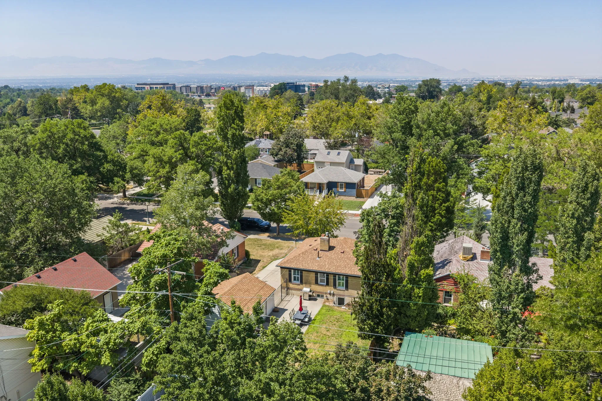 Aerial view showcasing this residence nestled on a tree-lined lot with mature landscaping, copper roof accents, and multiple structures including a detached garage