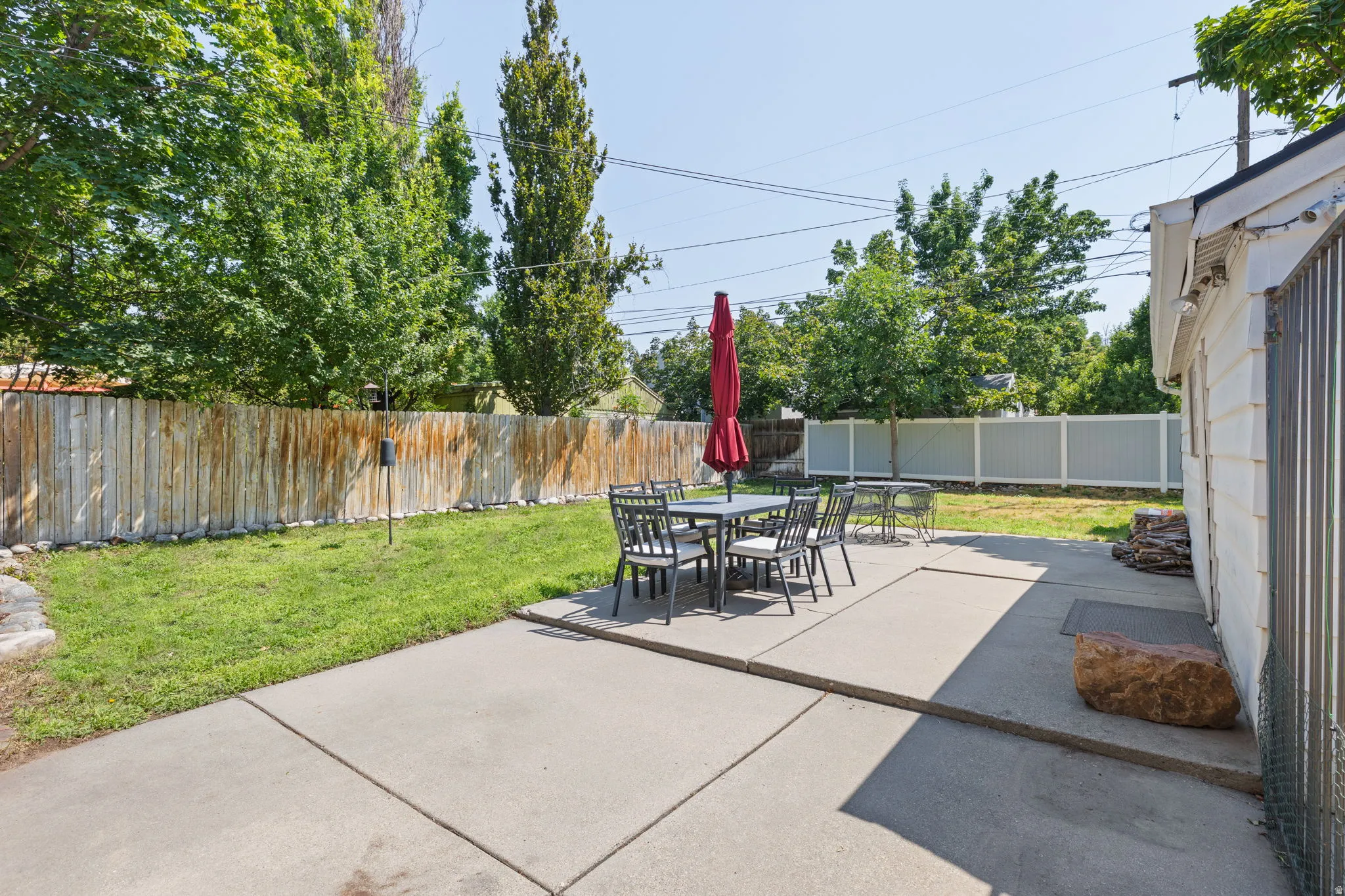 Spacious backyard oasis featuring a large concrete patio, mature shade trees, and a fenced perimeter