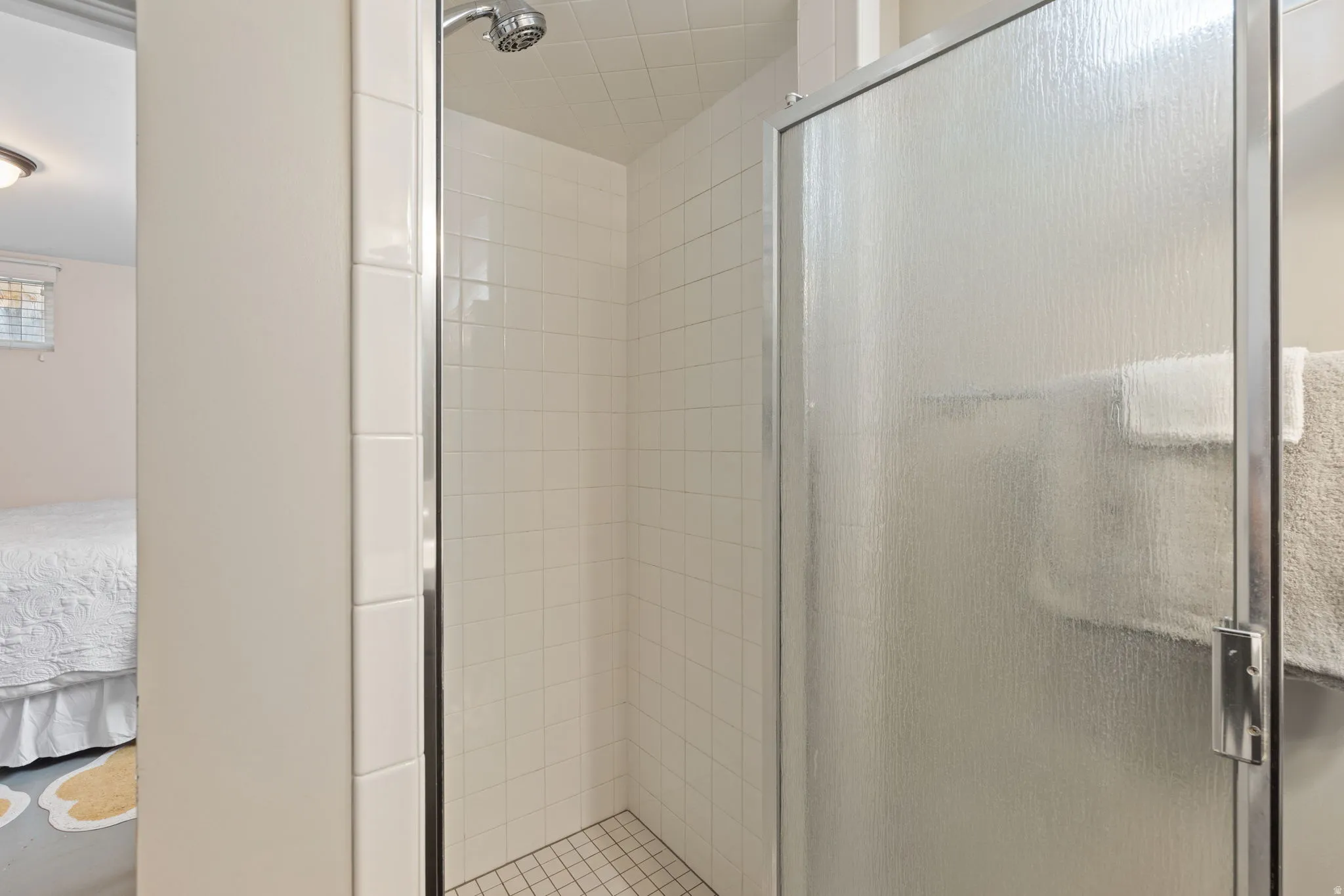 Shower enclosure featuring textured glass door with chrome frame, white tile surround, and mosaic tile floor