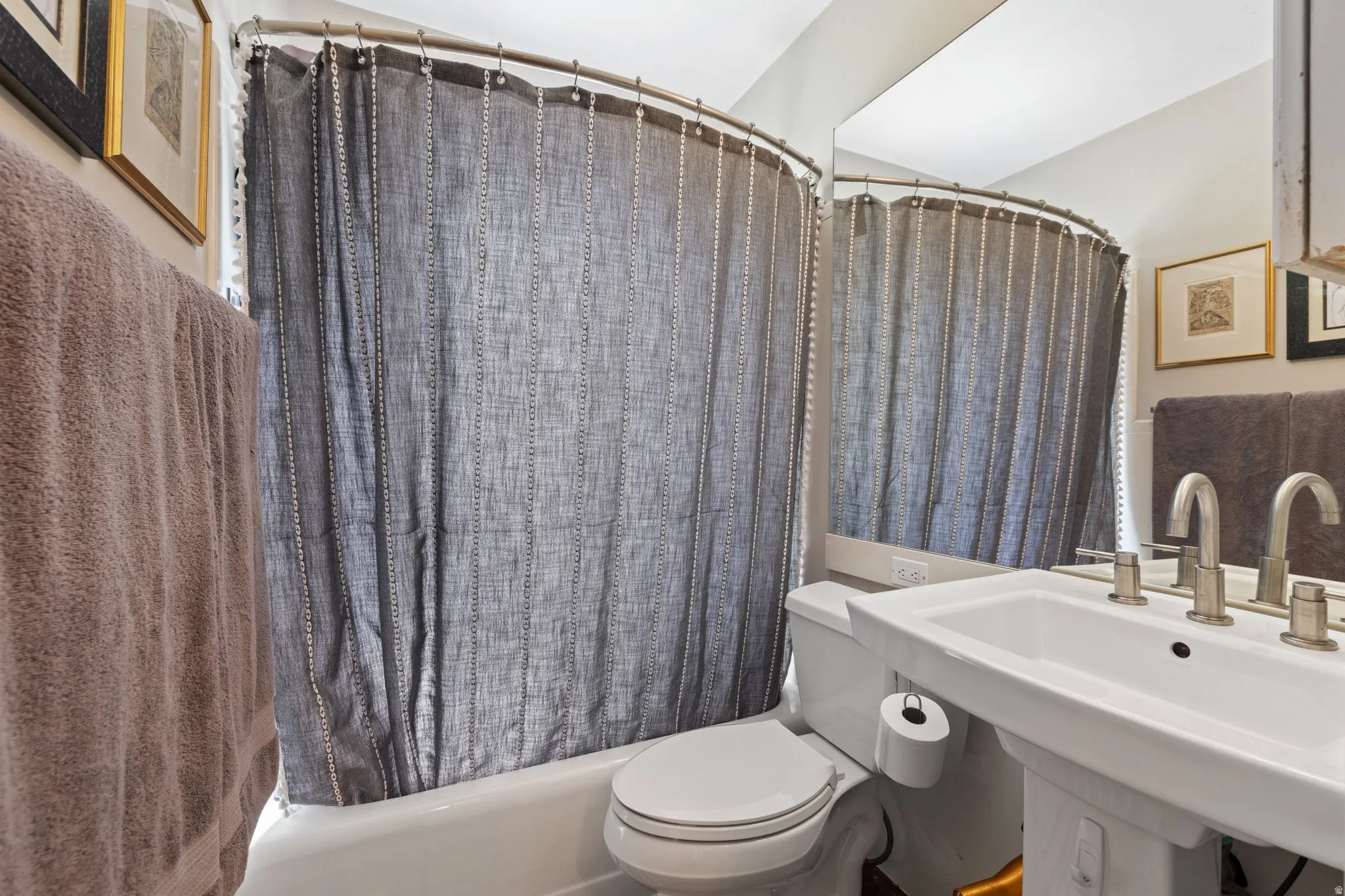 Bathroom featuring a pedestal sink with a dual-handle faucet, a toilet, and a shower/tub combination with a curved shower rod