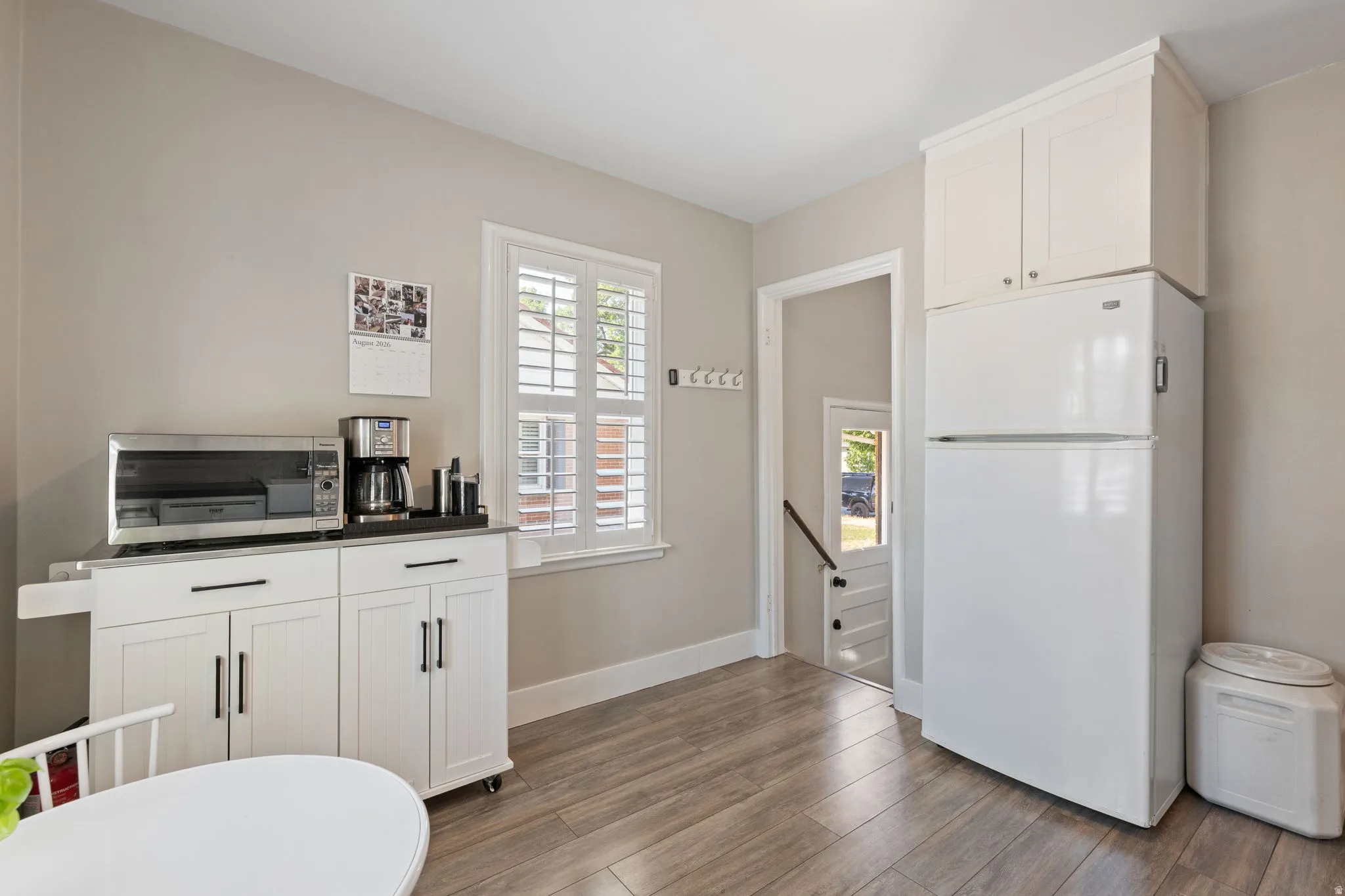 Bright interior space featuring a window with white plantation shutters, light gray wall paint, and wood-finish flooring