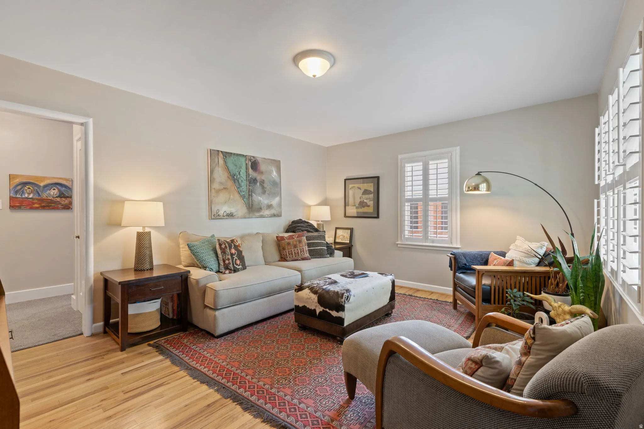 Living area featuring light wood-finish flooring, neutral wall paint, and white window shutters