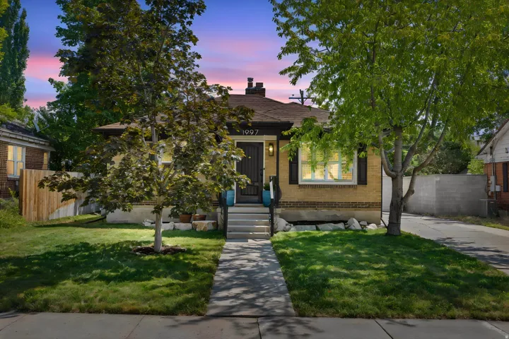 Brick exterior with dark shutters, paved driveway, and mature landscaping
