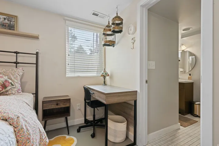 Bedroom featuring a window with blinds, wood-finish flooring, and a doorway opening to a bathroom with tile flooring and a vanity