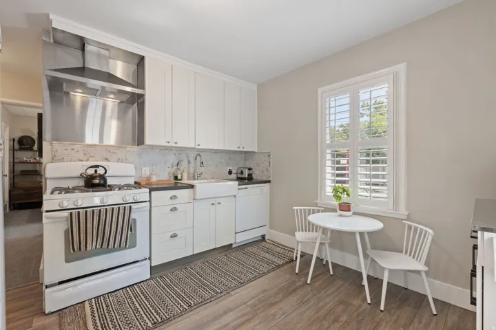Kitchen featuring white cabinetry, dark countertops, a farmhouse sink, stainless steel range hood, and wood-finish flooring