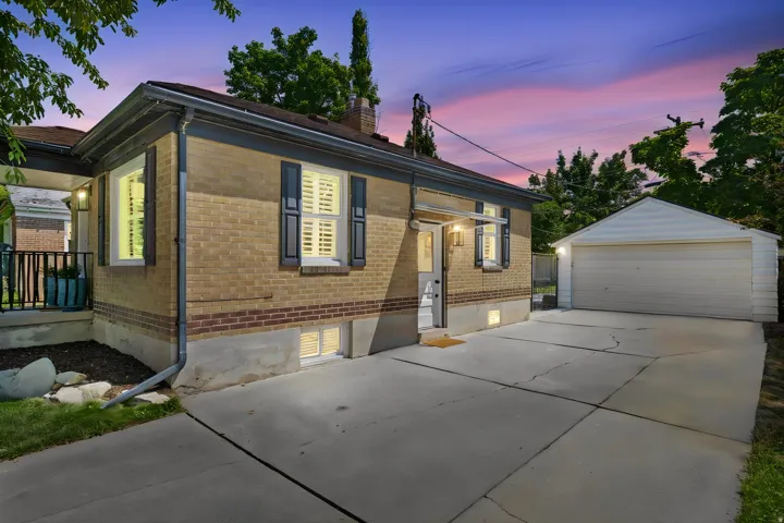 Brick exterior with dark shutters, covered entry, basement windows, and a detached garage with a concrete driveway