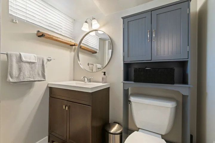 Bathroom featuring a wood-finish vanity with an integrated sink and chrome faucet, a circular wall-mounted mirror, and a two-light vanity fixture