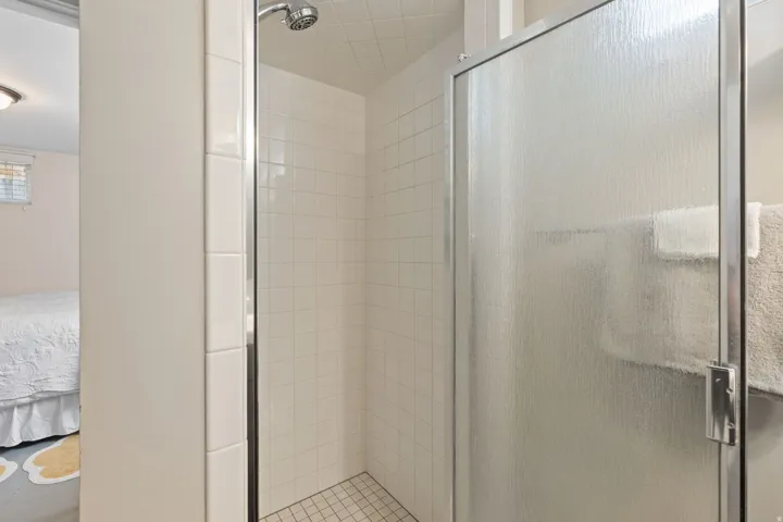 Shower enclosure featuring textured glass door with chrome frame, white tile surround, and mosaic tile floor