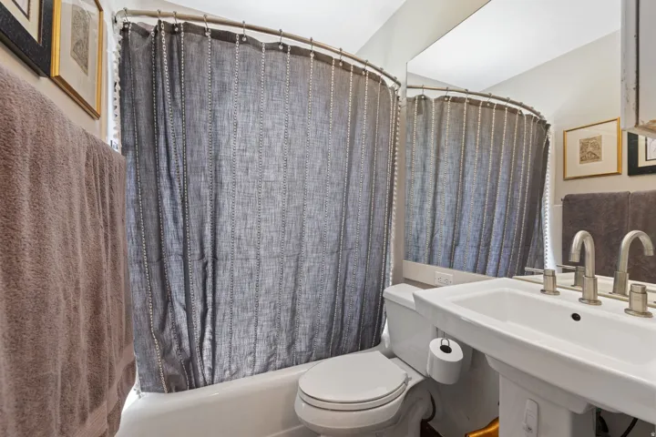 Bathroom featuring a pedestal sink with a dual-handle faucet, a toilet, and a shower/tub combination with a curved shower rod
