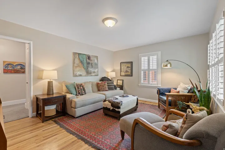 Living area featuring light wood-finish flooring, neutral wall paint, and white window shutters