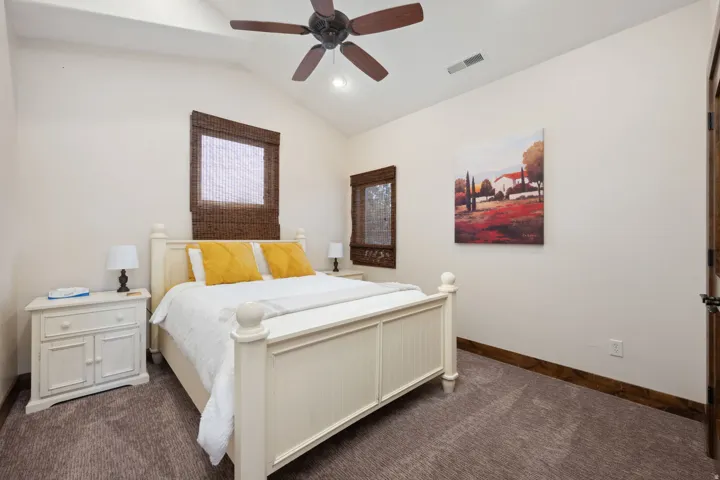 Vaulted ceiling bedroom featuring a ceiling fan, dual windows with woven wood shades, and a coordinating wood door