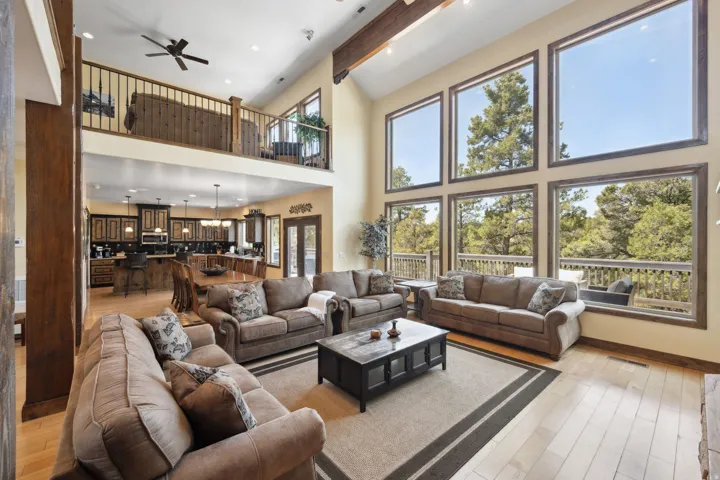 Soaring two-story living room showcasing floor-to-ceiling windows, exposed wood beams, and a ceiling fan