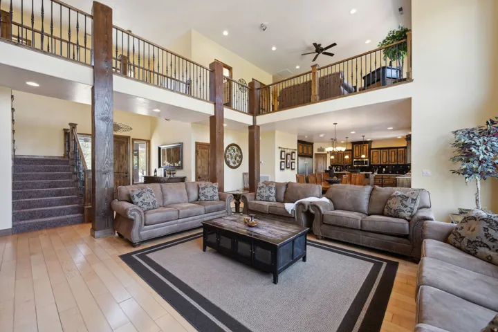 Soaring two-story living room featuring exposed timber columns, hardwood flooring with contrasting border inlay, and a coffered ceiling with recessed lighting