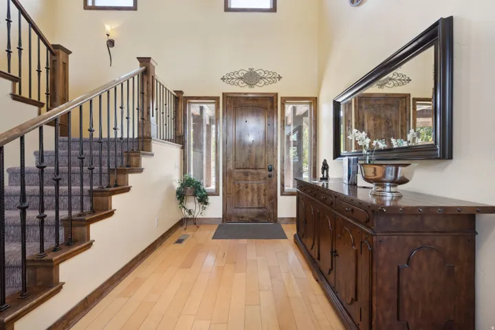Elegant foyer showcasing a curved staircase with dark metal railings and warm wood treads, wide-plank wood-finish flooring, and soaring ceilings with transom windows