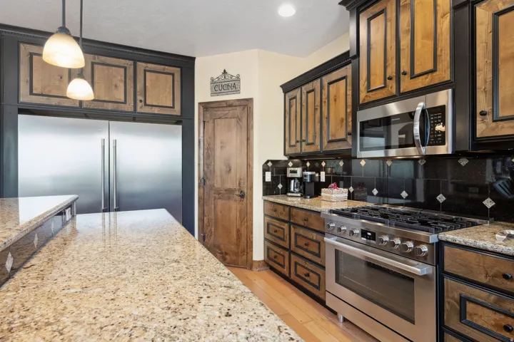 Chef's kitchen showcasing wood-finish cabinetry with black hardware, stainless steel appliances including a professional-grade range, granite countertops, pendant lighting, and a generous island with seating