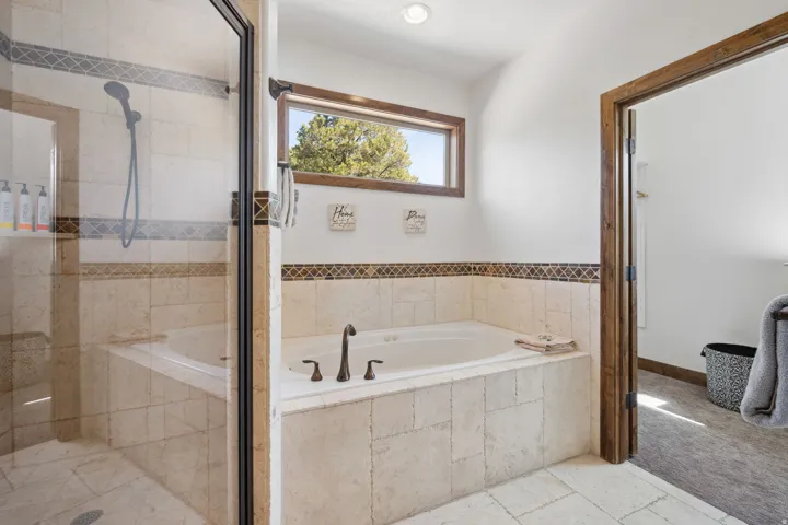Bathroom featuring a built-in soaking tub, a separate glass-enclosed shower, a wood-framed window, and decorative tile accents