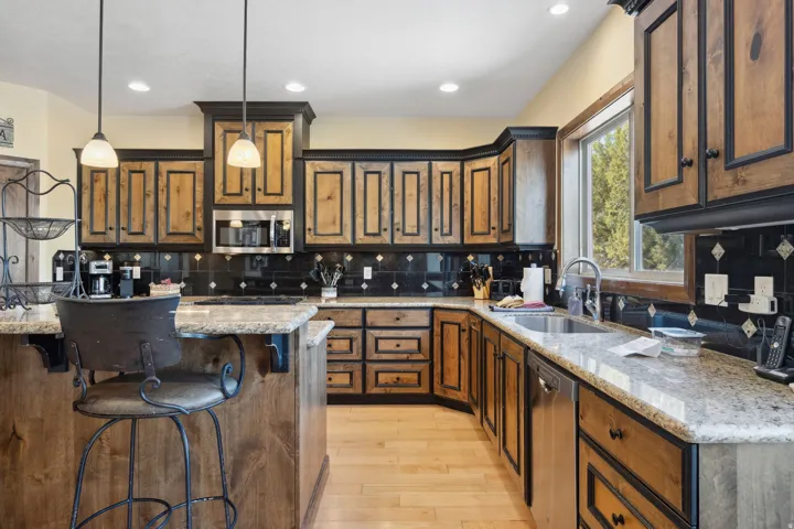 Chef's kitchen featuring rich wood cabinetry with detailed panel doors, stainless steel appliances, and expansive granite countertops with waterfall edge detailing
