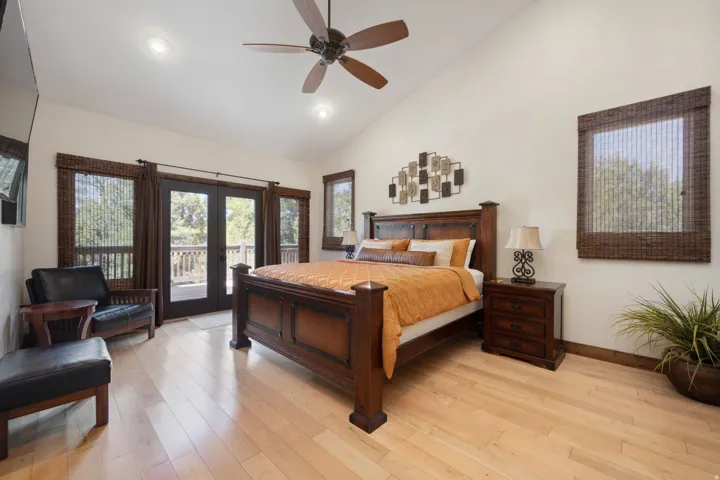 Spacious primary bedroom featuring rich wood-finish flooring, a substantial wood-frame bed, dual nightstands, and abundant natural light from multiple French doors and transom windows