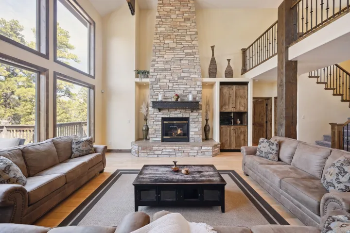 Living area featuring a floor-to-ceiling stone fireplace, soaring vaulted ceilings, wood-finish flooring, a full-height window wall, and a built-in wood-finish cabinet