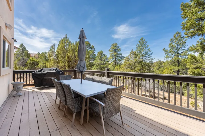 Expansive composite deck with wood-finish flooring and white balusters, featuring a dining table with seating for four, lounge chairs, and a freestanding umbrella