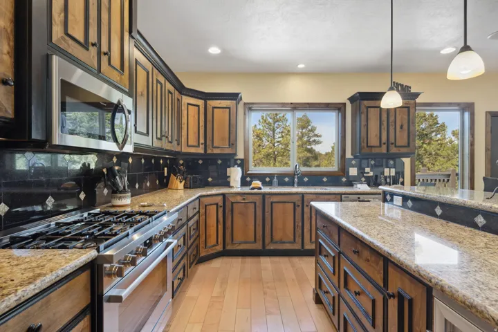 Chef's kitchen featuring custom wood-finish cabinetry with contrasting black trim, granite countertops, stainless steel gas cooktop, and built-in stainless steel appliances
