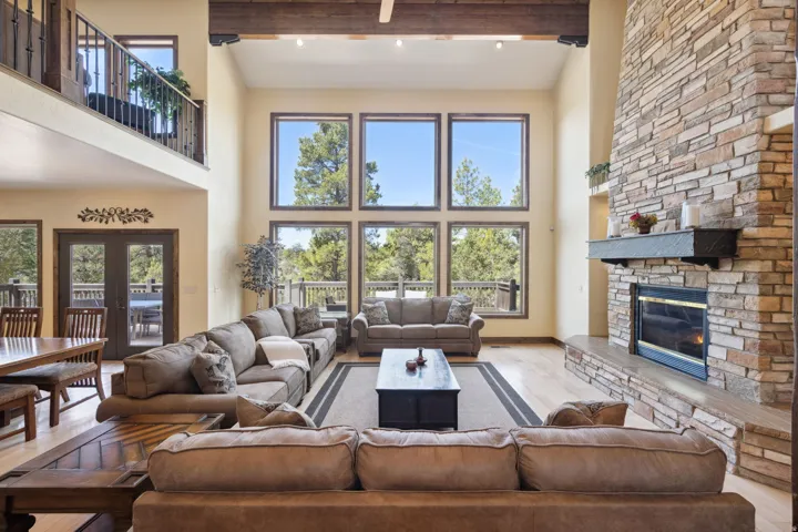 Vaulted ceiling living area featuring a stacked stone fireplace with a dark mantel, wood-finish flooring, and a bank of tall windows