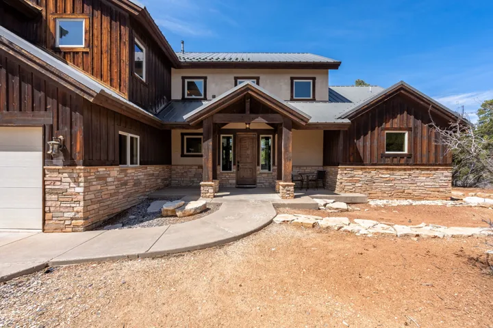Striking exterior featuring wood siding, stacked stone accents, a metal roof, an inviting covered entry, and a concrete pathway
