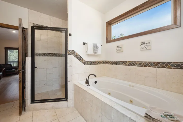 Tiled bathroom featuring a built-in jetted tub, a separate glass-enclosed shower, and a high horizontal window with wood trim