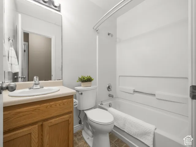 Bathroom featuring a light wood-finish vanity with a built-in sink, a wall-mounted mirror, a two-bulb vanity light fixture, and a tub/shower combination with a white surround