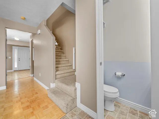 Entryway featuring wood-finish flooring, a carpeted staircase, and a visible powder room with a toilet and patterned floor tile