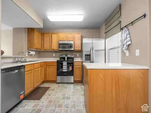 Spacious kitchen featuring warm wood cabinetry, stainless steel appliances including a built-in microwave and gas range, white quartz countertops, a large center island with wood-finish base, and patterned tile flooring throughout