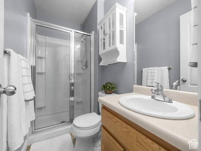 Bright and functional bathroom featuring a wood-finish vanity with an oval sink and chrome faucet, ceramic tile flooring, and a glass-enclosed shower stall with chrome fixtures