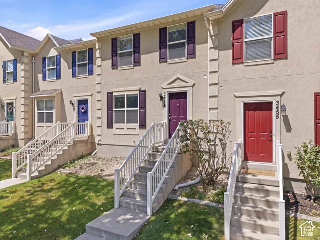 Townhome exterior featuring stucco siding, multiple windows with contrasting shutters, concrete entry stairs with white railings, and individual front doors