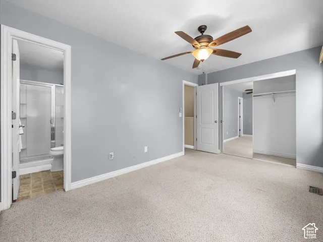 Spacious primary bedroom featuring neutral gray walls, plush carpeting, a ceiling fan with integrated lighting, and mirrored sliding closet doors