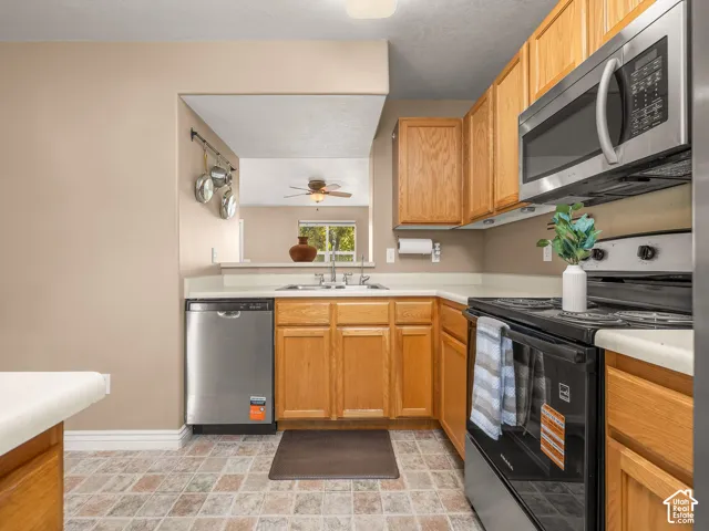Efficient kitchen featuring wood cabinetry, stainless steel appliances including a built-in microwave and double wall ovens, a ceramic tile floor with a neutral color palette, and a compact layout with ample counter and storage space