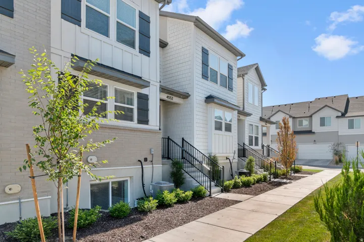 Modern two-story residence featuring a clean white exterior with board-and-batten siding, multi-pane windows, and a welcoming front entry with black metal railings
