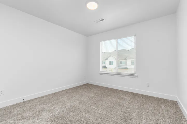 Spacious room featuring neutral carpeting, white painted walls, a flush-mount ceiling light, and a window with blinds